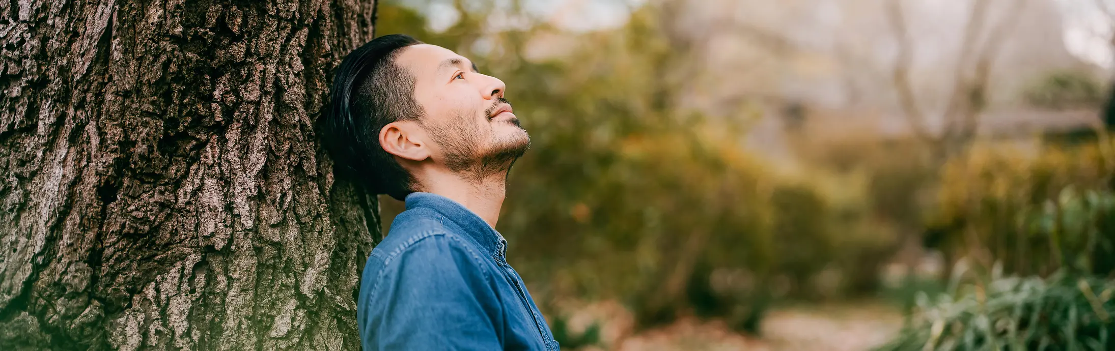 本を片手に木にもたれかかる男性